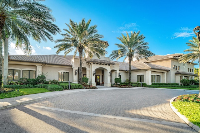 mediterranean / spanish home with curved driveway, stucco siding, and a tile roof