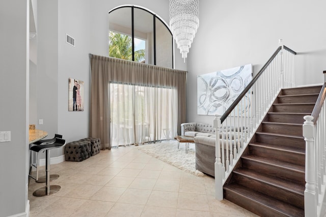 entrance foyer with visible vents, a high ceiling, stairway, tile patterned floors, and a notable chandelier