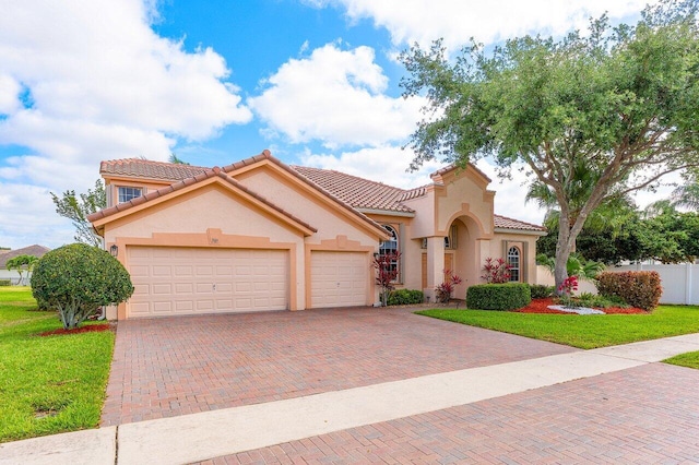 mediterranean / spanish house featuring stucco siding, decorative driveway, a front yard, and a garage