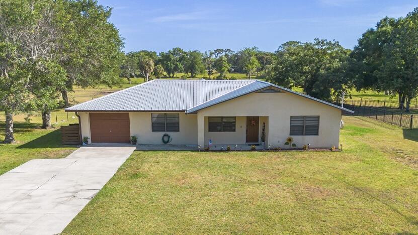 440 NE 138th St, Okeechobee, FL 34972 - view of front of property featuring fence, a garage, stucco siding, a front yard, and driveway