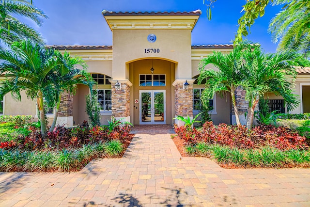 15688 Italian Cypress Way, Wellington, FL 33414 - view of exterior entry featuring french doors, a tile roof, stone siding, and stucco siding