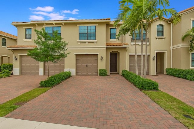 view of property with a tiled roof, a garage, driveway, and stucco siding