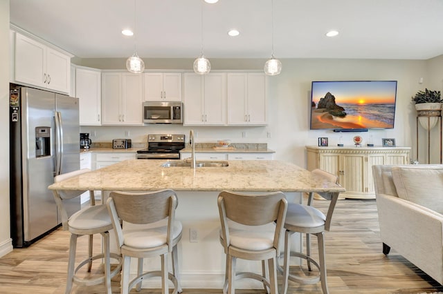 kitchen featuring a kitchen breakfast bar, appliances with stainless steel finishes, a sink, white cabinets, and light wood-style flooring