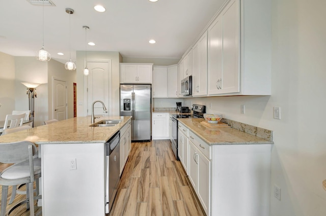kitchen featuring a breakfast bar, light wood-type flooring, white cabinetry, a sink, and appliances with stainless steel finishes