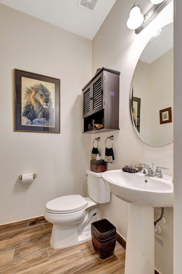 half bath with baseboards, toilet, wood finished floors, and visible vents