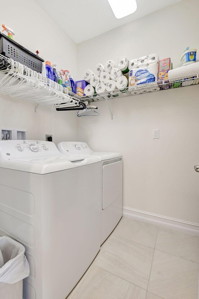 clothes washing area featuring laundry area, baseboards, light tile patterned flooring, and washer and dryer