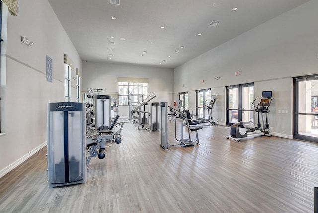 exercise room with baseboards, recessed lighting, wood finished floors, and a towering ceiling