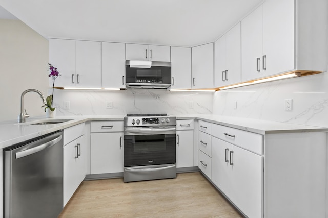 kitchen featuring decorative backsplash, light wood-style floors, white cabinets, a sink, and stainless steel appliances