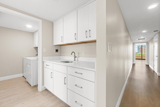 clothes washing area with cabinet space, baseboards, a sink, and light wood-style floors