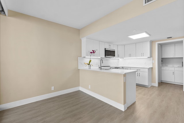 kitchen featuring light wood-type flooring, a peninsula, stainless steel microwave, and tasteful backsplash
