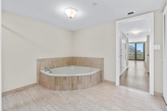 full bathroom featuring visible vents, baseboards, a bath, and wood finished floors