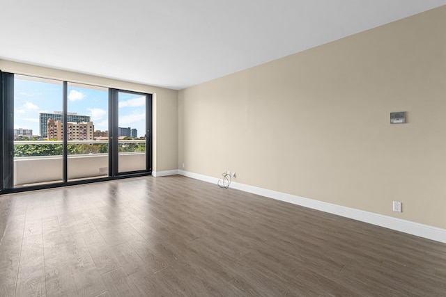 empty room featuring baseboards, a view of city, and dark wood-type flooring