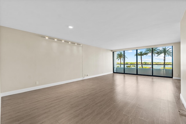 unfurnished room featuring baseboards, floor to ceiling windows, and wood finished floors