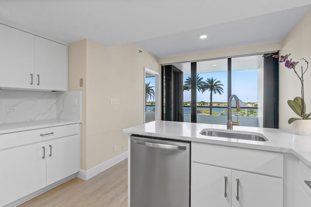kitchen featuring stainless steel dishwasher, light countertops, a sink, light wood-style flooring, and backsplash
