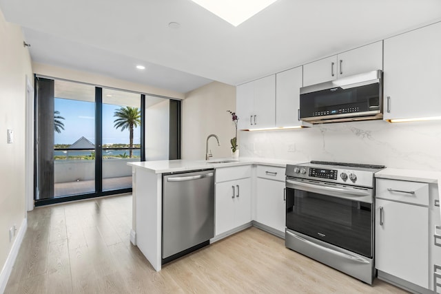 kitchen featuring backsplash, appliances with stainless steel finishes, light wood-type flooring, a sink, and a peninsula