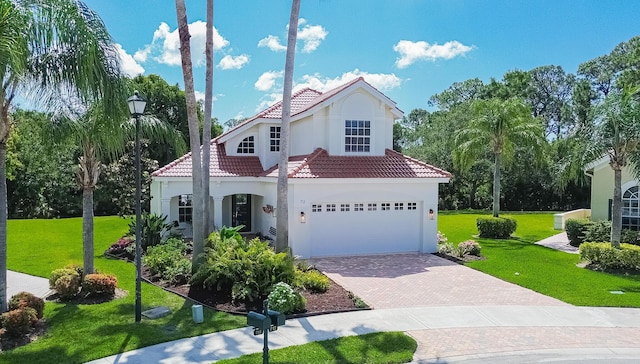 mediterranean / spanish-style house featuring a tile roof, a garage, stucco siding, a front yard, and decorative driveway