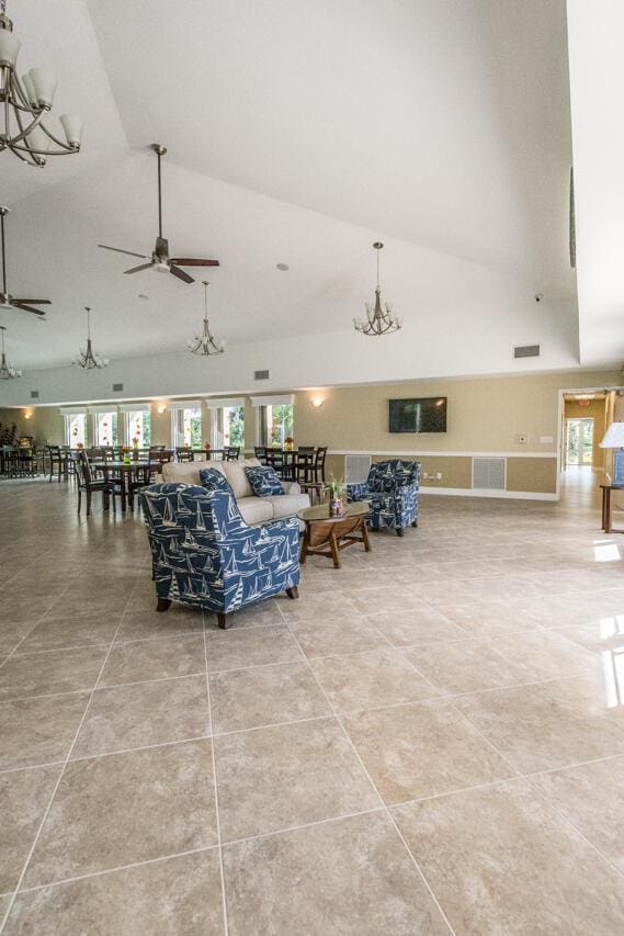 living area with high vaulted ceiling, plenty of natural light, ceiling fan with notable chandelier, and tile patterned floors