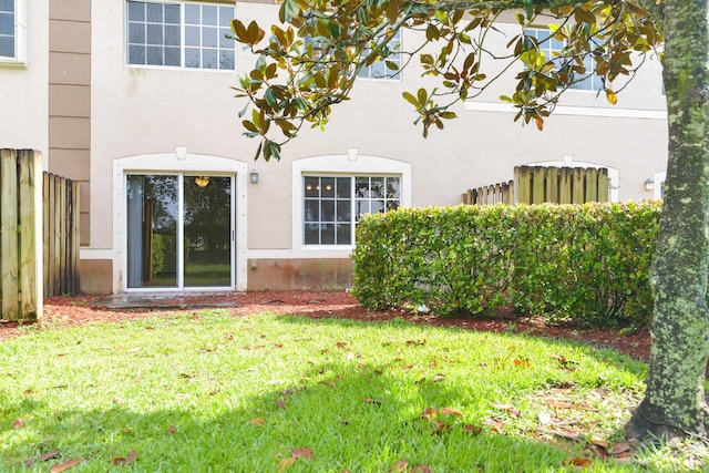 rear view of house with a lawn, fence, and stucco siding