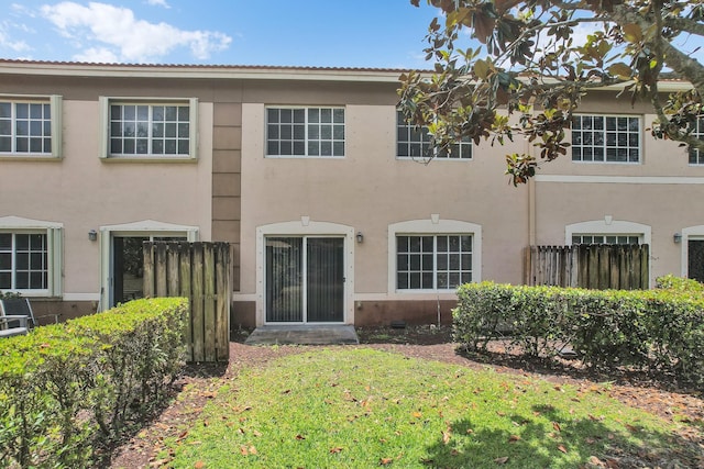 rear view of property featuring stucco siding, fence, and a lawn