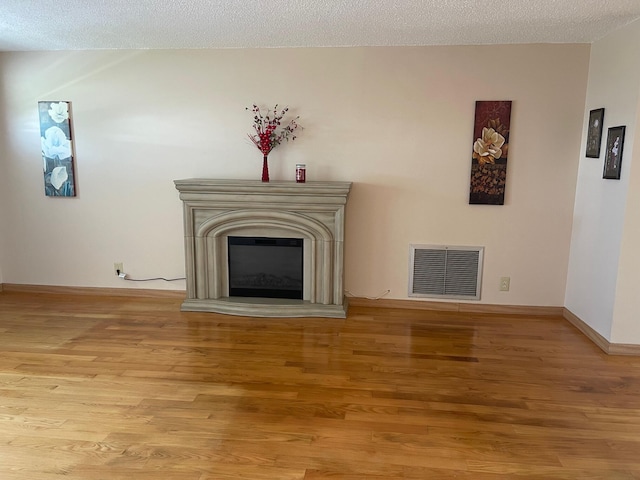 unfurnished living room with light wood-type flooring, visible vents, baseboards, and a glass covered fireplace