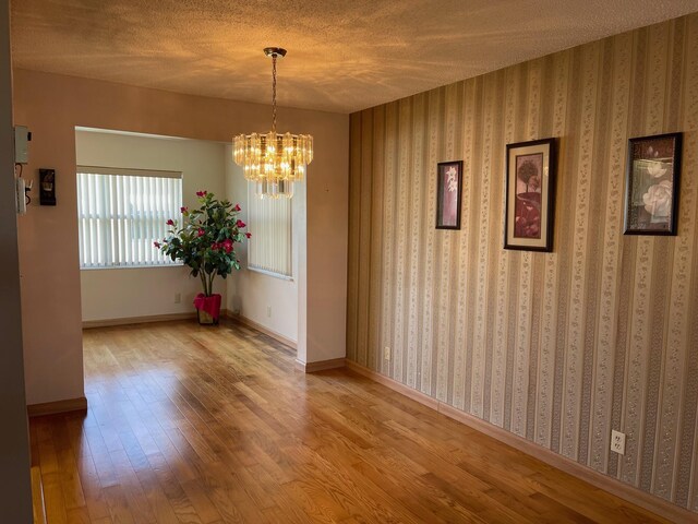 unfurnished dining area with a chandelier, baseboards, wood finished floors, and a textured ceiling