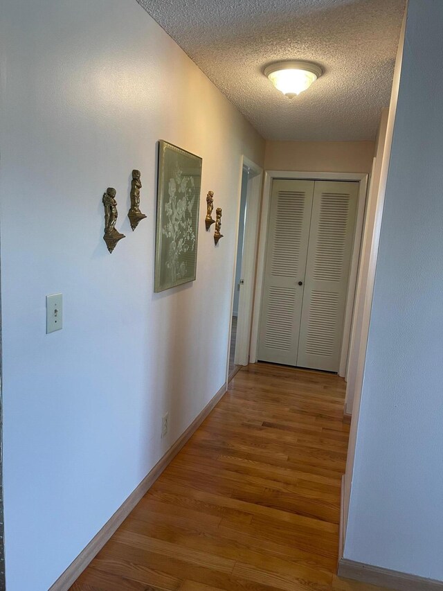 corridor featuring a textured ceiling, wood finished floors, and baseboards