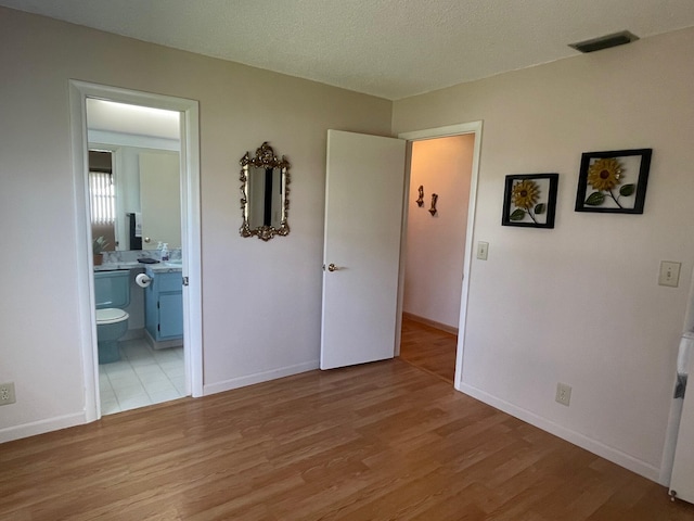 bedroom featuring ensuite bath, visible vents, light wood finished floors, and baseboards