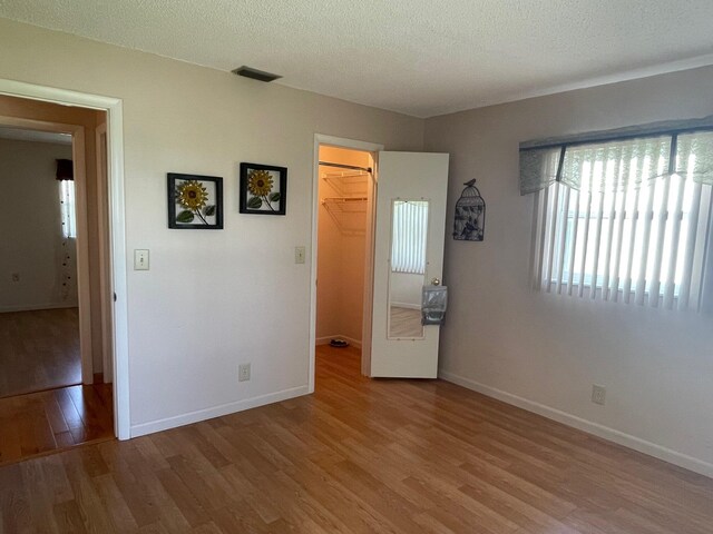 unfurnished bedroom featuring wood finished floors, visible vents, a spacious closet, and baseboards