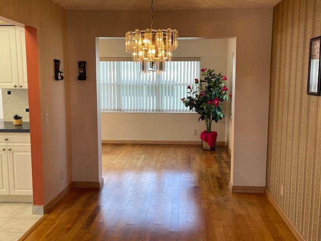unfurnished dining area featuring a chandelier, wallpapered walls, light wood-style flooring, and baseboards