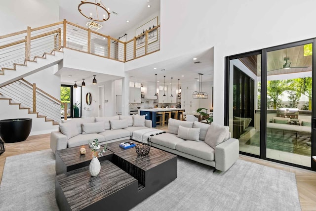 living room featuring visible vents, stairs, a notable chandelier, and a high ceiling
