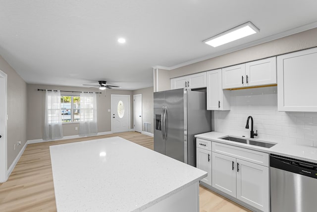 kitchen with a sink, light wood-style floors, backsplash, white cabinetry, and appliances with stainless steel finishes