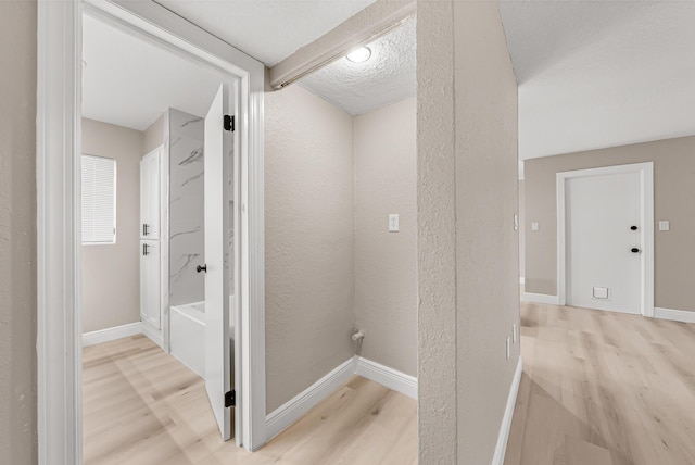 hall featuring light wood-style floors, a textured wall, and baseboards