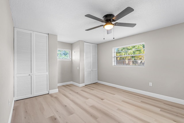 unfurnished bedroom with light wood finished floors, a textured ceiling, baseboards, ceiling fan, and multiple closets