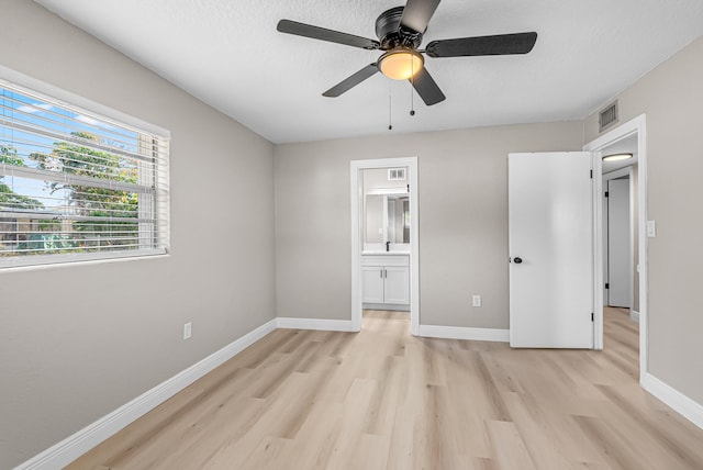 unfurnished bedroom with connected bathroom, visible vents, baseboards, light wood finished floors, and a ceiling fan