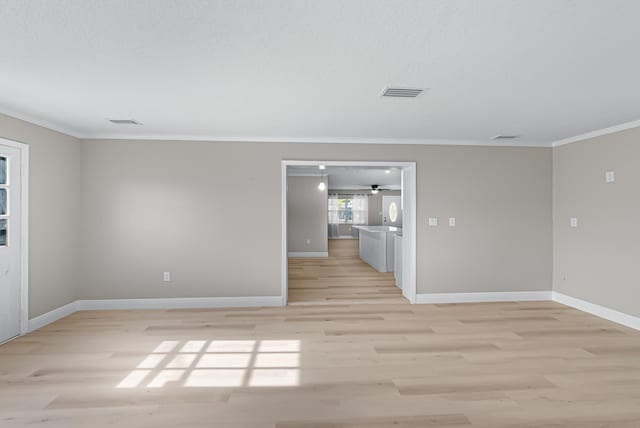 empty room with ornamental molding, visible vents, light wood-style flooring, and baseboards