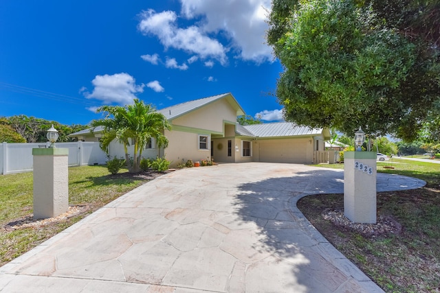 ranch-style home featuring an attached garage, driveway, metal roof, and stucco siding