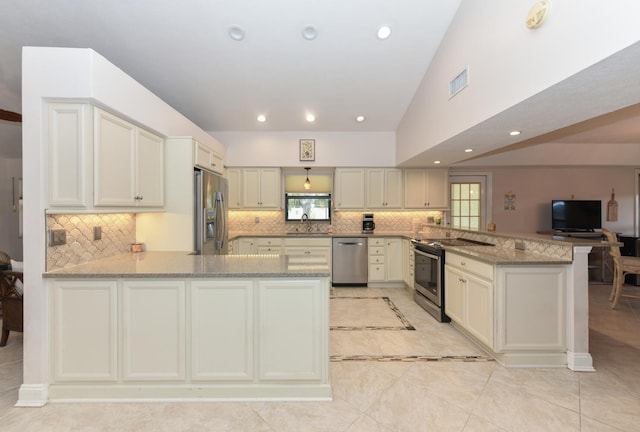 kitchen with appliances with stainless steel finishes, a peninsula, a sink, light stone counters, and backsplash