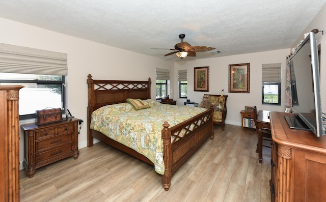 bedroom featuring light wood-style flooring, multiple windows, a textured ceiling, baseboards, and ceiling fan