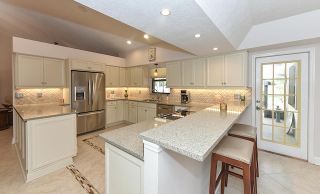 kitchen featuring appliances with stainless steel finishes, a peninsula, vaulted ceiling, a sink, and light stone counters