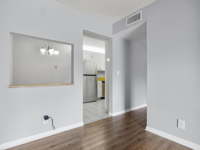 empty room featuring a chandelier, wood finished floors, a textured ceiling, and baseboards