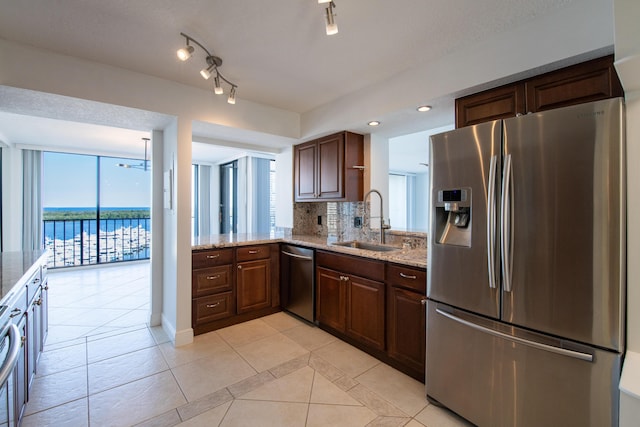 kitchen featuring tasteful backsplash, light stone countertops, light tile patterned floors, appliances with stainless steel finishes, and a sink