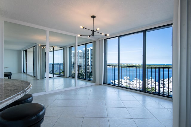 spare room featuring tile patterned floors, a chandelier, a water view, and expansive windows