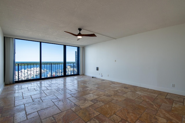 spare room with a textured ceiling, stone tile flooring, ceiling fan, a water view, and floor to ceiling windows