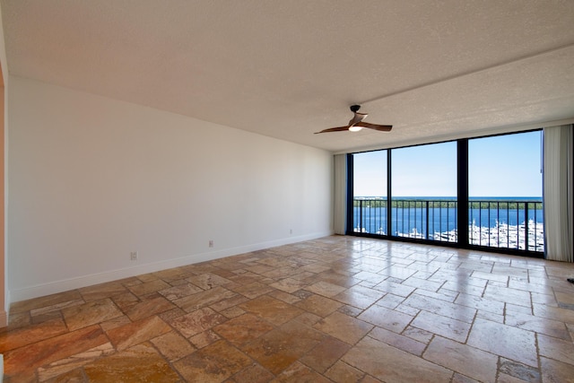empty room featuring stone tile floors, ceiling fan, expansive windows, baseboards, and a textured ceiling