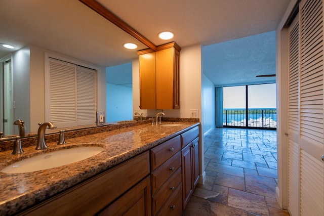 full bath with a closet, a sink, double vanity, and stone tile flooring