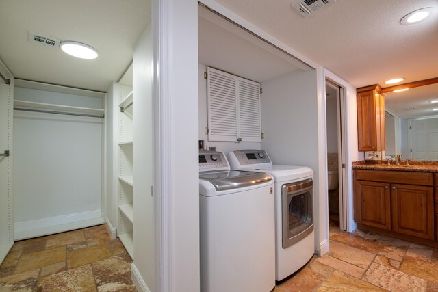 washroom with visible vents, stone tile flooring, washing machine and clothes dryer, and a sink