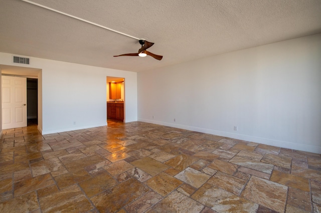 unfurnished room with stone tile flooring, ceiling fan, visible vents, baseboards, and a textured ceiling