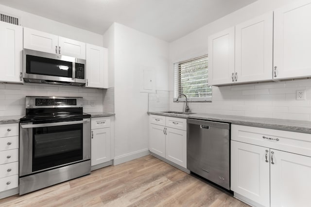 kitchen with light wood finished floors, a sink, appliances with stainless steel finishes, and tasteful backsplash