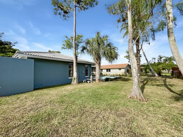 rear view of property featuring stucco siding, a tile roof, and a yard