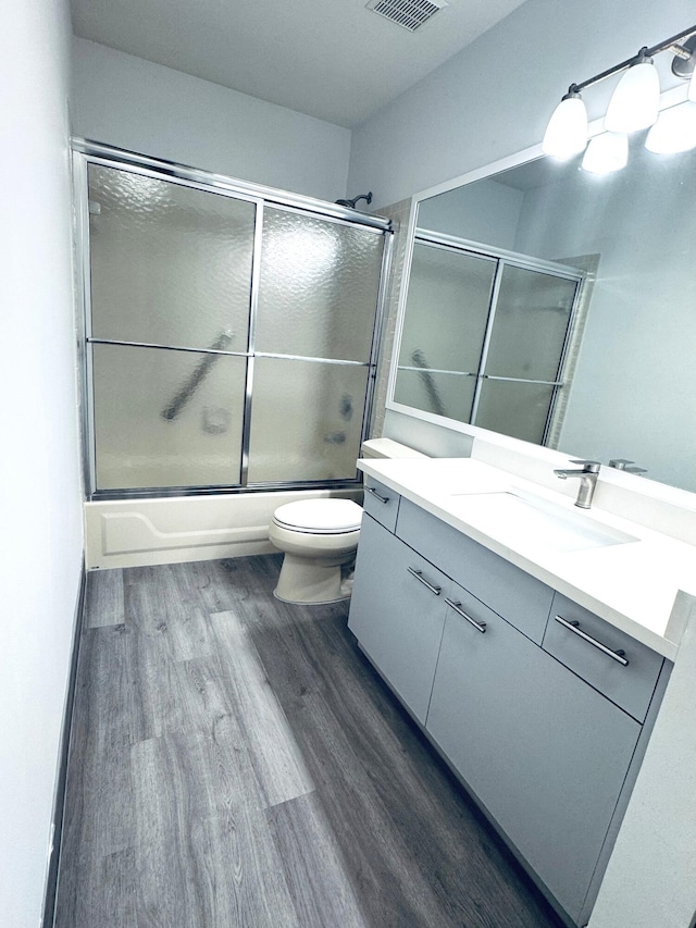 bathroom with wood finished floors, shower / bath combination with glass door, toilet, vanity, and visible vents